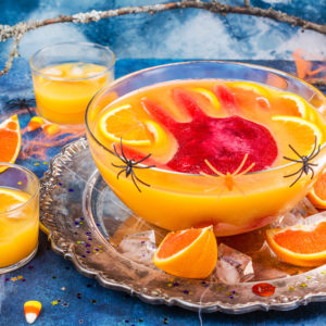 Ghoul's orange punch with bloody ice hand in a glass bowl on dark halloween background